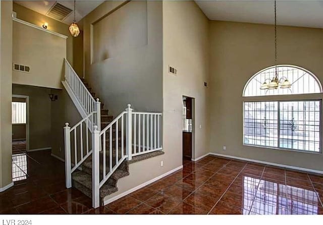 foyer with a towering ceiling, a chandelier, and dark tile patterned flooring