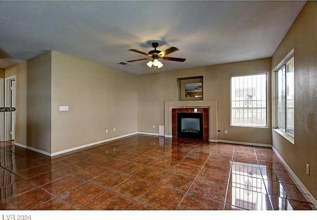 unfurnished living room featuring a tile fireplace, ceiling fan, and dark tile patterned flooring