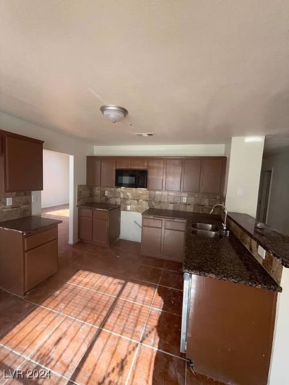 kitchen with tasteful backsplash, kitchen peninsula, sink, and dark tile patterned flooring