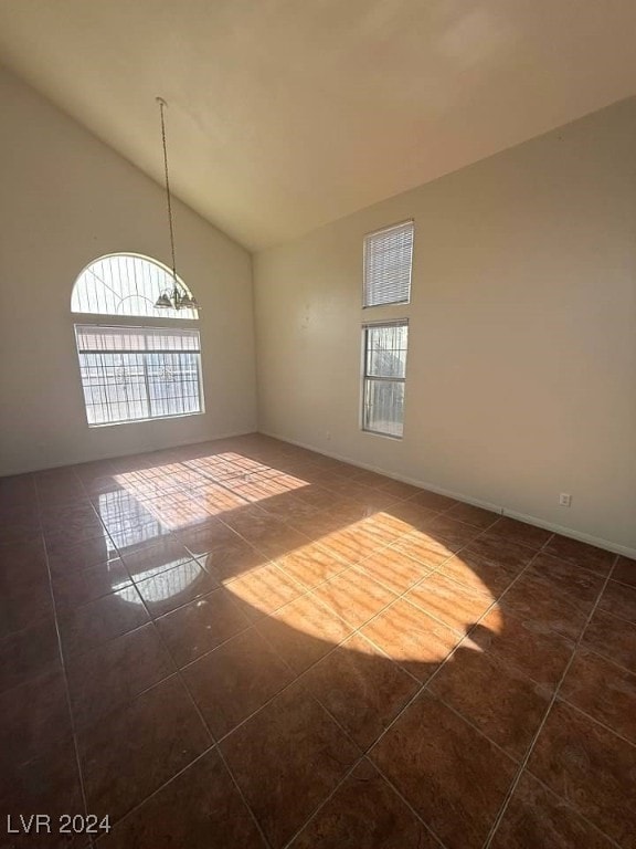 spare room with a chandelier, vaulted ceiling, dark tile patterned floors, and a healthy amount of sunlight