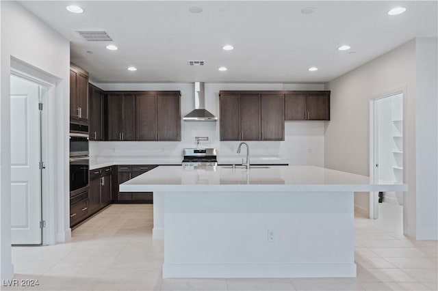 kitchen with a center island with sink, appliances with stainless steel finishes, sink, wall chimney exhaust hood, and dark brown cabinets