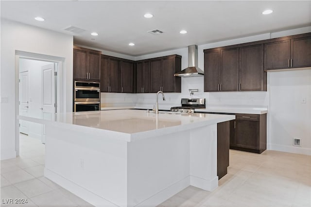 kitchen featuring appliances with stainless steel finishes, sink, wall chimney exhaust hood, an island with sink, and dark brown cabinetry