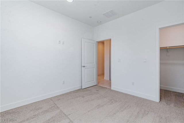 unfurnished bedroom featuring a spacious closet, light colored carpet, and a closet