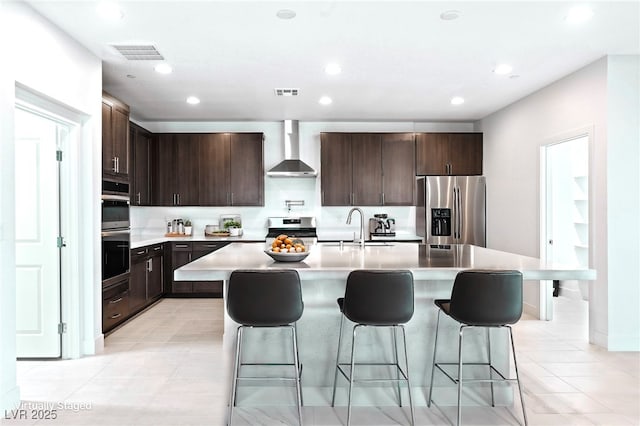 kitchen featuring a center island with sink, sink, stainless steel appliances, and wall chimney range hood