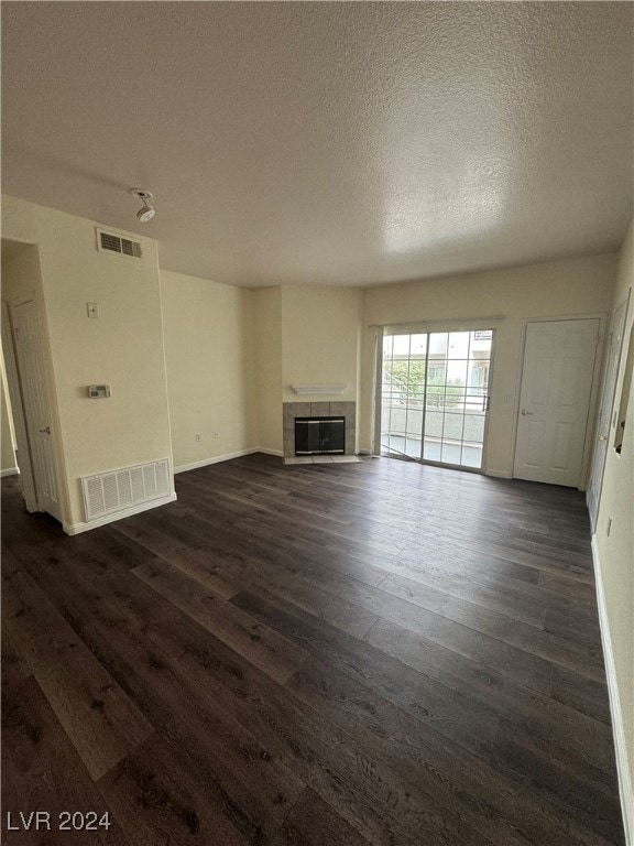 unfurnished living room featuring a textured ceiling, a tiled fireplace, and dark hardwood / wood-style flooring