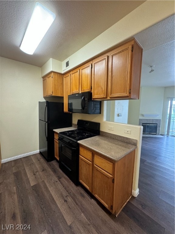 kitchen featuring dark wood-type flooring, a tiled fireplace, black appliances, and a textured ceiling