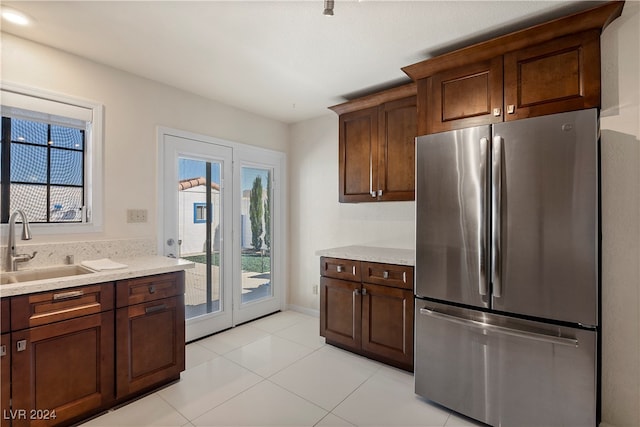 kitchen featuring light stone counters, dark brown cabinetry, stainless steel refrigerator, sink, and light tile patterned floors