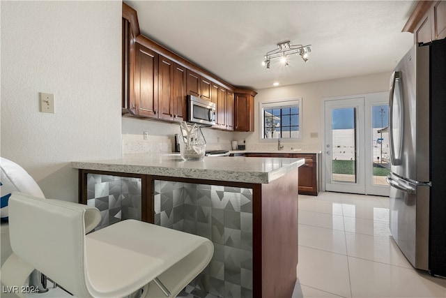 kitchen featuring light tile patterned flooring, sink, kitchen peninsula, stainless steel appliances, and a breakfast bar