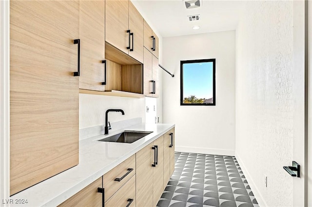 kitchen featuring light brown cabinetry, sink, and light stone countertops