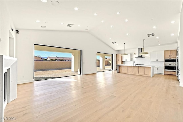 unfurnished living room featuring sink, high vaulted ceiling, a healthy amount of sunlight, and light wood-type flooring