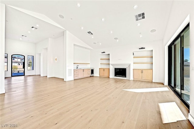 unfurnished living room featuring sink, built in shelves, light hardwood / wood-style floors, and a healthy amount of sunlight