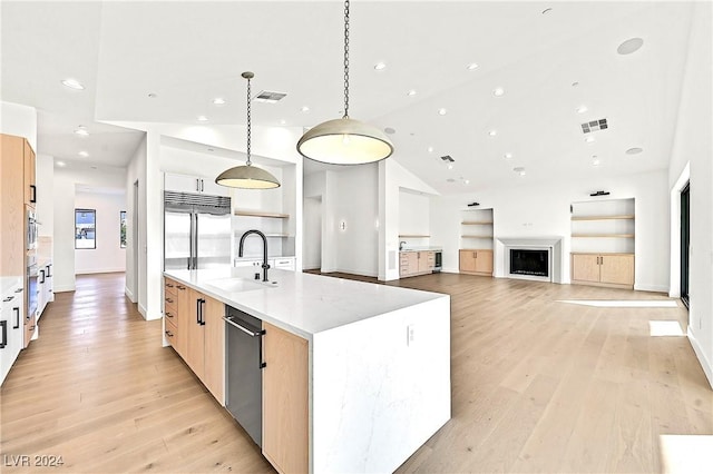 kitchen with light wood-type flooring, decorative light fixtures, sink, and a large island with sink