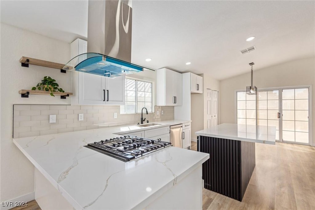 kitchen featuring pendant lighting, vaulted ceiling, island range hood, light stone counters, and white cabinetry