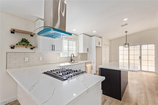 kitchen featuring pendant lighting, vaulted ceiling, island range hood, light stone counters, and white cabinetry