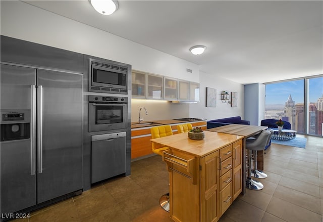 kitchen featuring dark tile patterned flooring, expansive windows, built in appliances, sink, and a kitchen bar