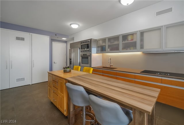 kitchen with appliances with stainless steel finishes, a kitchen bar, dark tile patterned floors, and sink