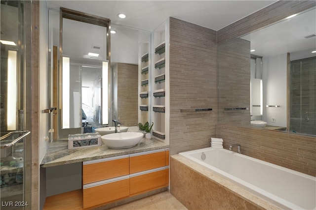 bathroom featuring tiled tub, vanity, tile walls, and tile patterned floors