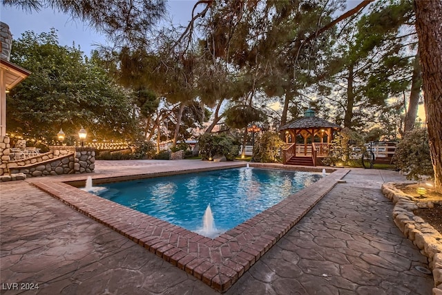 pool at dusk with a gazebo, a patio, and pool water feature