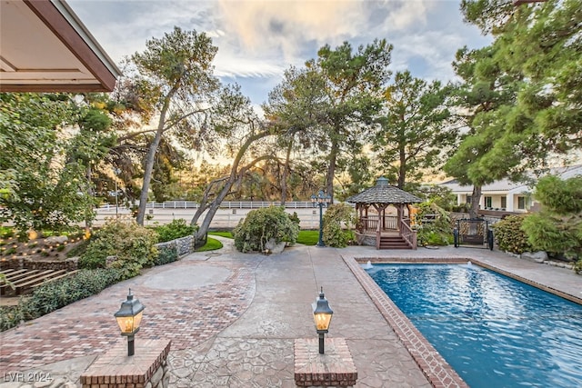 pool at dusk featuring a gazebo and a patio area