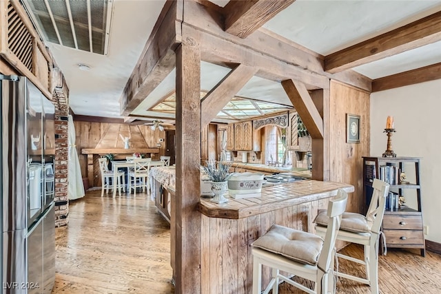 kitchen with ceiling fan, beamed ceiling, light hardwood / wood-style flooring, tile countertops, and a breakfast bar