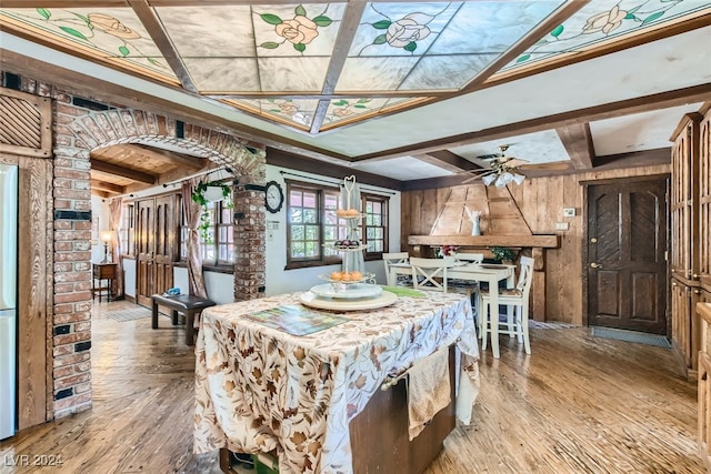 dining space with ceiling fan, beamed ceiling, wooden walls, and hardwood / wood-style flooring