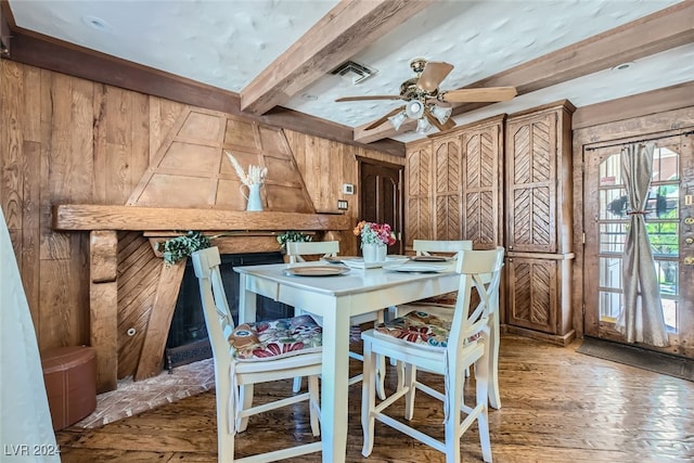 dining area featuring ceiling fan, beamed ceiling, wood walls, and hardwood / wood-style flooring