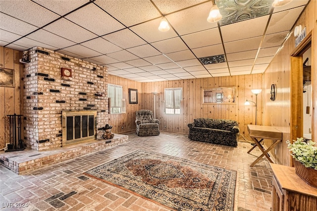 unfurnished living room with a brick fireplace, a drop ceiling, and wood walls