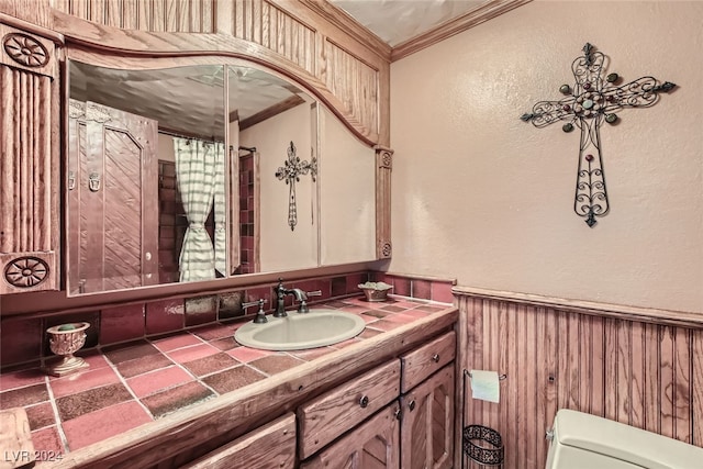 bathroom with wooden walls, crown molding, vanity, and toilet