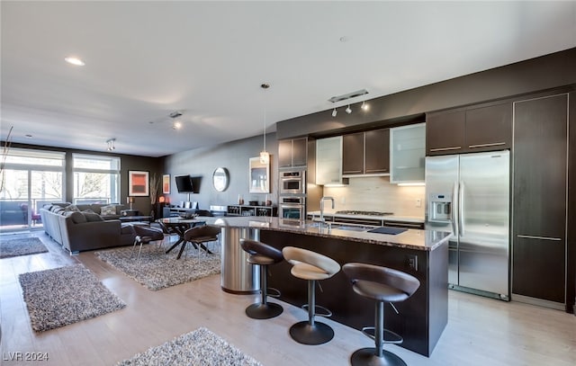 kitchen featuring a center island with sink, appliances with stainless steel finishes, light wood-type flooring, and a kitchen breakfast bar