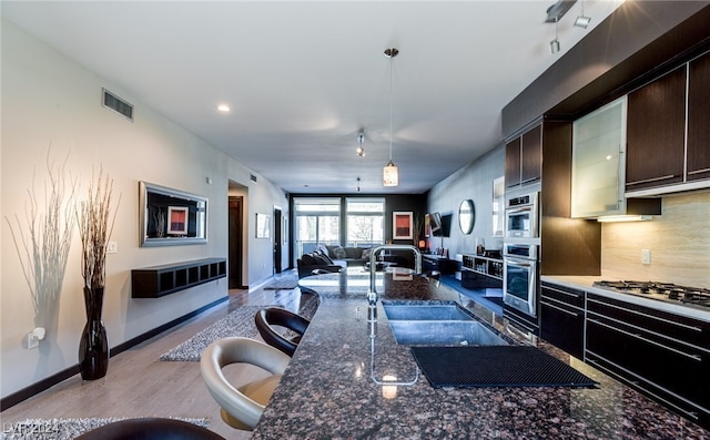 kitchen featuring pendant lighting, dark stone counters, dark brown cabinetry, appliances with stainless steel finishes, and a kitchen bar