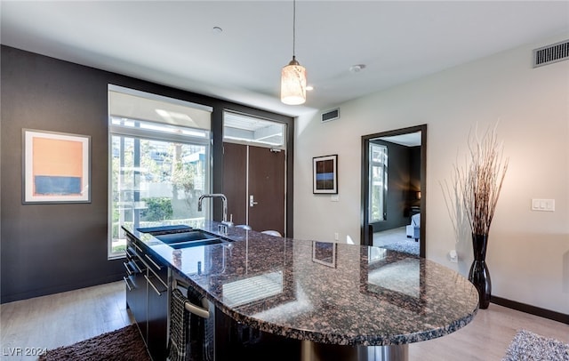 kitchen featuring an island with sink, dark stone countertops, sink, light hardwood / wood-style floors, and pendant lighting