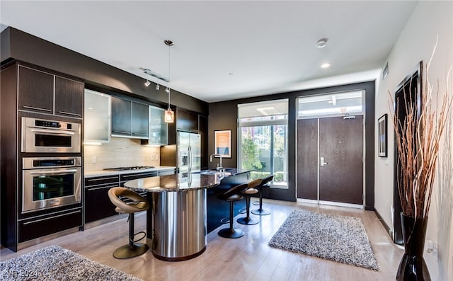 kitchen with light hardwood / wood-style floors, pendant lighting, a kitchen breakfast bar, a center island with sink, and appliances with stainless steel finishes