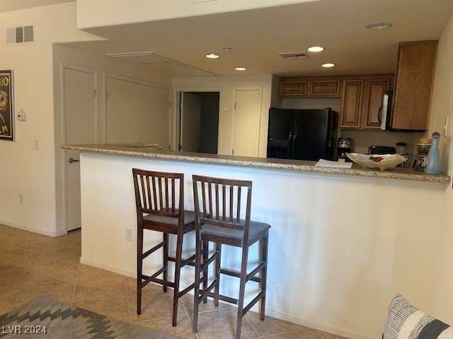 kitchen with light tile patterned floors, black fridge, a breakfast bar area, and kitchen peninsula