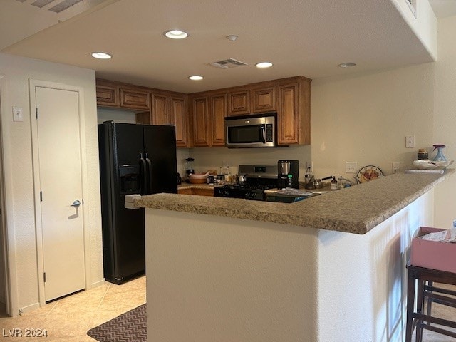 kitchen with light stone countertops, stainless steel appliances, light tile patterned flooring, kitchen peninsula, and a kitchen breakfast bar