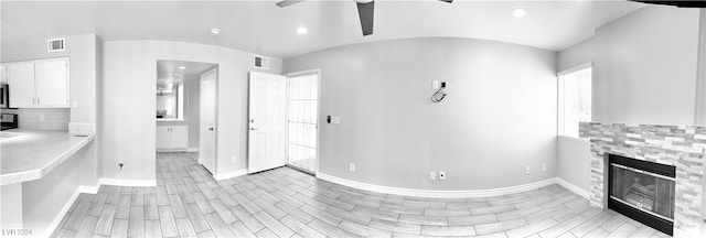 interior space with ceiling fan, a stone fireplace, light wood-type flooring, and white cabinets