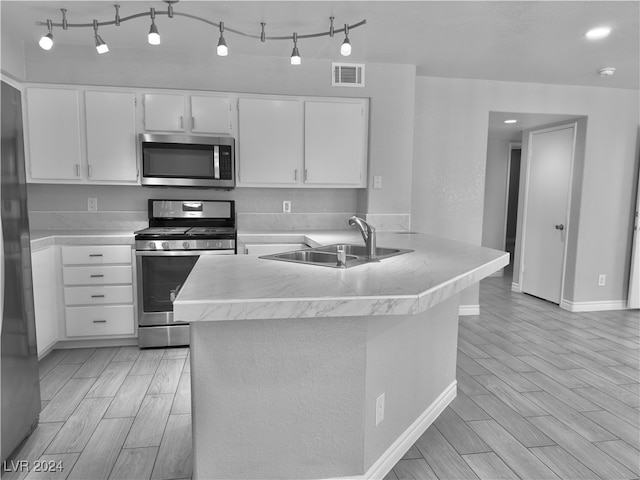 kitchen with kitchen peninsula, sink, white cabinets, appliances with stainless steel finishes, and light hardwood / wood-style floors