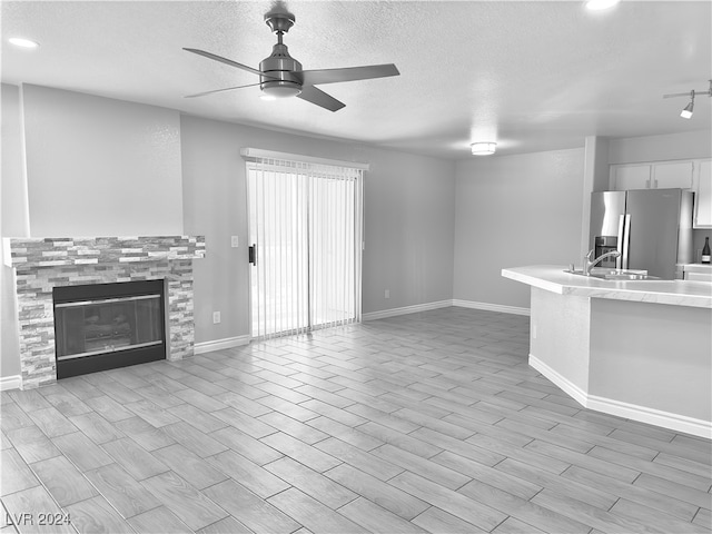 unfurnished living room with light hardwood / wood-style flooring, a textured ceiling, sink, and ceiling fan