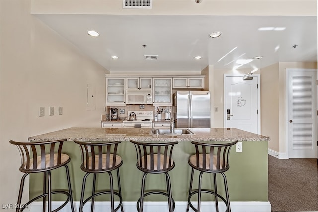 kitchen featuring white appliances, dark carpet, sink, light stone counters, and a kitchen bar