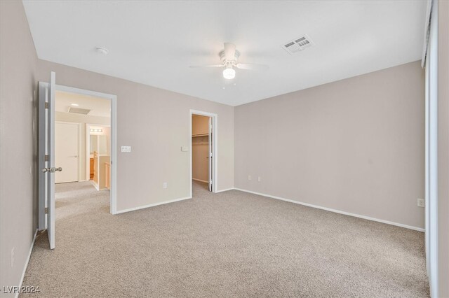 unfurnished bedroom with a spacious closet, ceiling fan, a closet, and light colored carpet