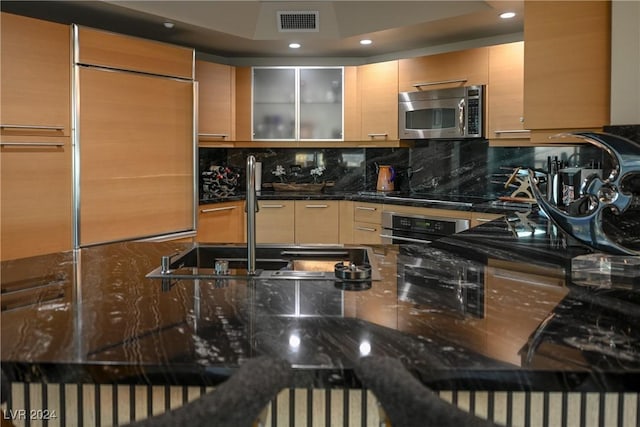 kitchen featuring decorative backsplash, dark stone countertops, sink, and appliances with stainless steel finishes