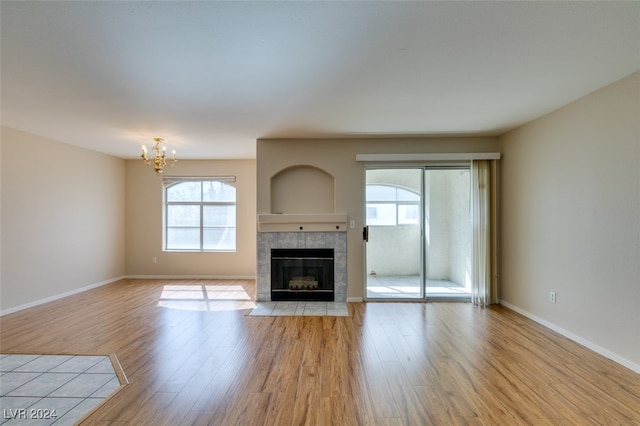 unfurnished living room featuring a notable chandelier, light wood-type flooring, and a tile fireplace