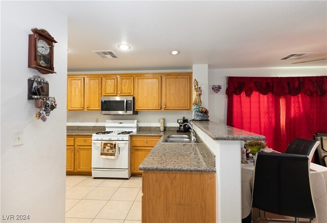 kitchen with light tile patterned floors, kitchen peninsula, sink, dark stone countertops, and white range with gas cooktop