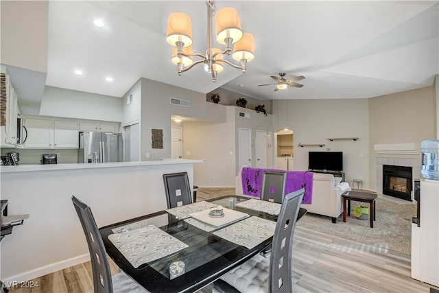 dining area featuring light wood-type flooring, ceiling fan with notable chandelier, and a fireplace