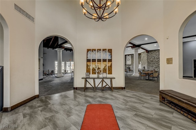 corridor featuring an inviting chandelier, ornate columns, and a towering ceiling