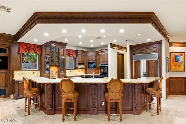 kitchen featuring light stone countertops, a kitchen bar, black appliances, and a large island with sink