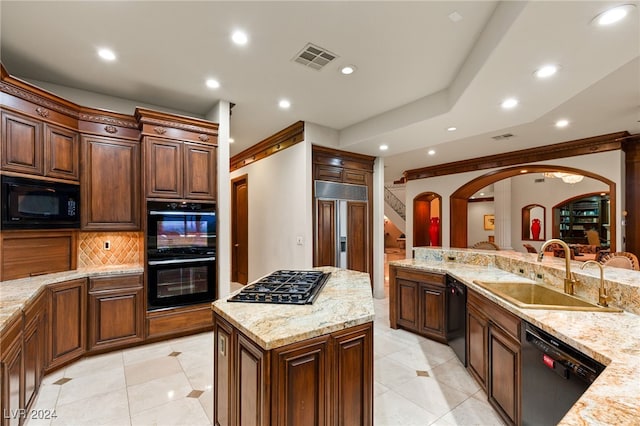 kitchen with a kitchen island, sink, light stone countertops, backsplash, and black appliances