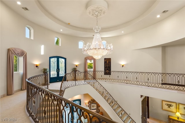 stairway with french doors, a raised ceiling, carpet floors, a towering ceiling, and a chandelier