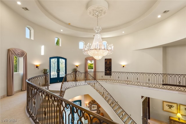 corridor with visible vents, an inviting chandelier, an upstairs landing, a towering ceiling, and french doors