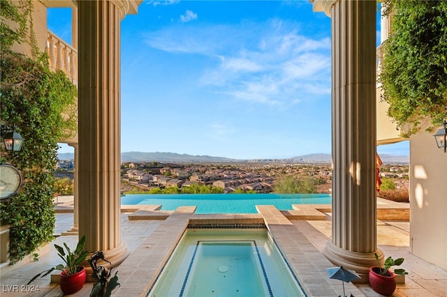 view of swimming pool featuring a mountain view, decorative columns, and an in ground hot tub