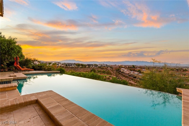 pool at dusk with a patio area and a mountain view